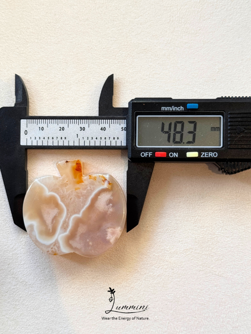 A polished agate stone pendant with natural banding in cream, white, and soft peach tones, shown under a digital caliper displaying 48.3 mm.