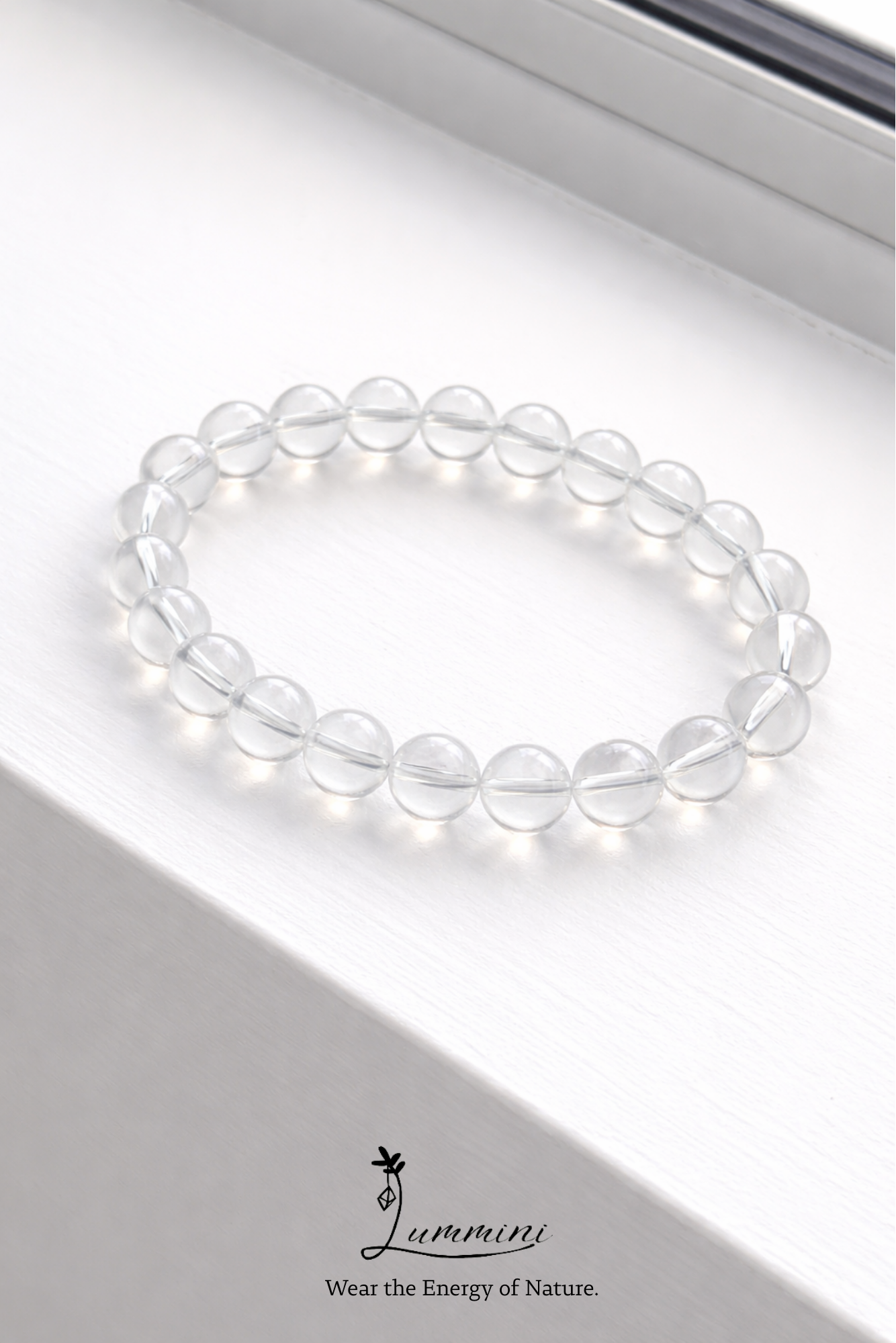 Clear beaded bracelet on a white surface with a brand logo at the bottom.
