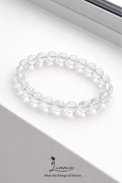 Clear beaded bracelet on a white surface with a brand logo at the bottom.
