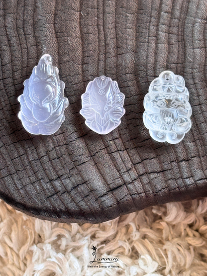 Three carved translucent white jade pendants with floral and animal motifs, arranged on a dark textured wood slice with a beige shag rug underneath.